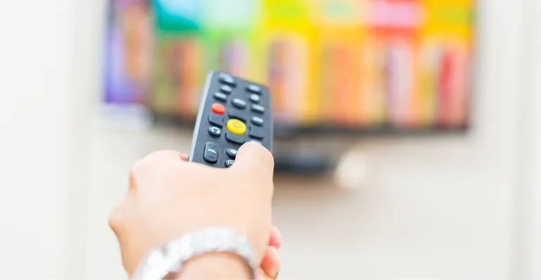 Pessoa apontando controle remoto para a TV, representando o uso de antena digital para acesso a canais de TV