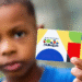 Criança segurando cartão do Programa Bolsa Família, com fundo desfocado.