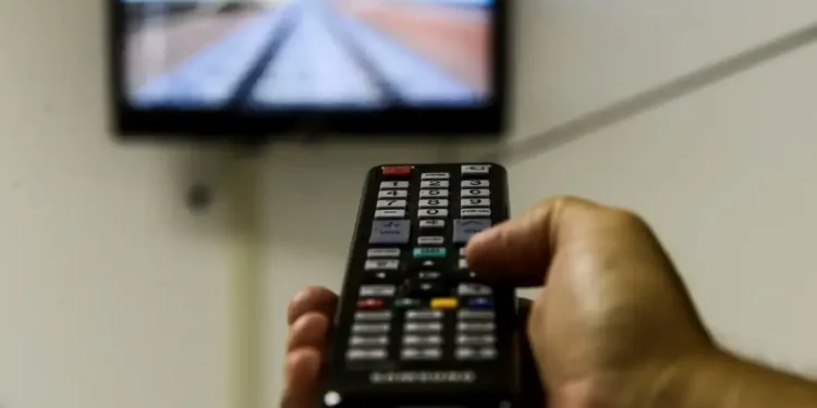 Pessoa apontando controle remoto para uma TV ligada, representando o uso de antena digital para assistir canais em HD gratuitamente.