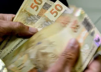 Notas de 50 reais sendo contadas, relacionadas ao consignado para trabalhadores CLT e motoristas de aplicativos.