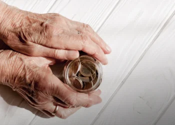 Mãos de idoso segurando pote com moedas sobre mesa clara