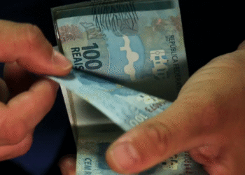 Mãos segurando notas de 100 reais com foco no valor, simbolizando o aumento do salário mínimo para R$ 2,2 mil.