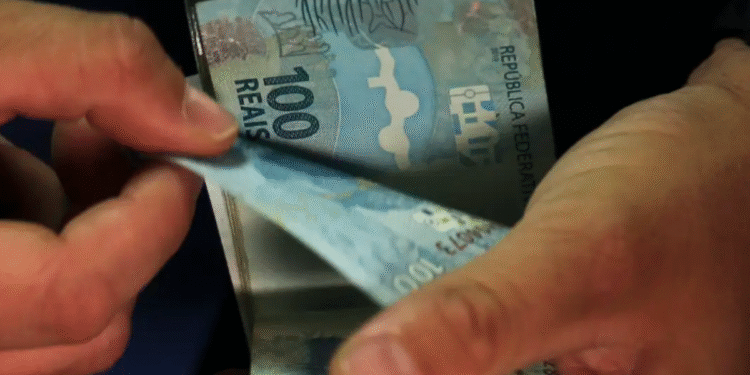 Mãos segurando notas de 100 reais com foco no valor, simbolizando o aumento do salário mínimo para R$ 2,2 mil.