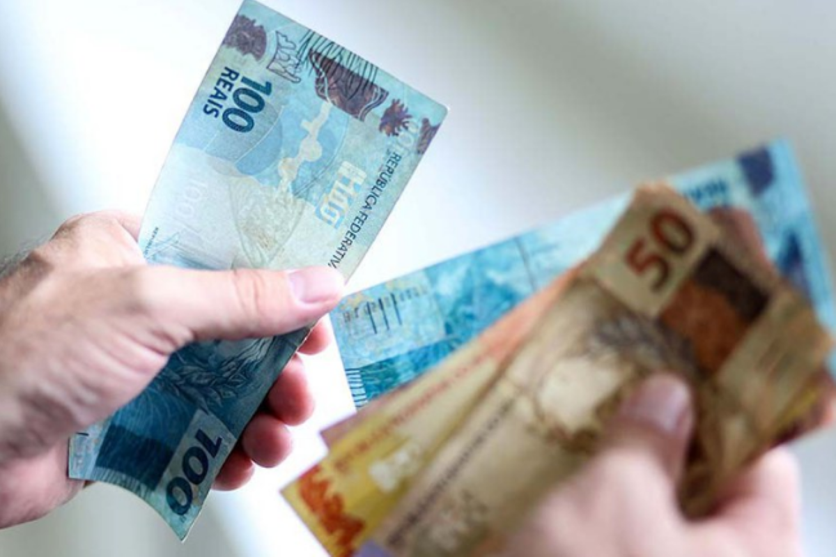 Notas de dinheiro em mãos, representando o pagamento do Bolsa Família