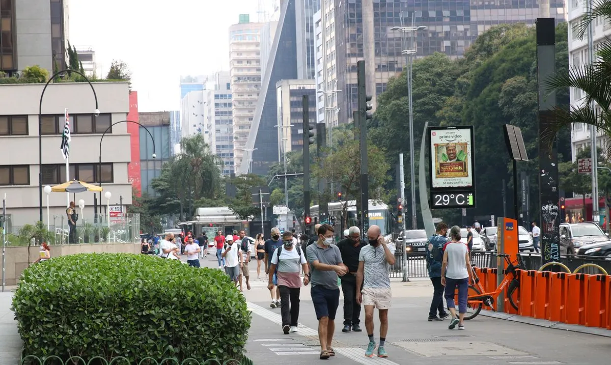 Imagem de pessoas caminhando em uma avenida movimentada de uma grande cidade, com destaque para as condições climáticas e o planejamento urbano.
