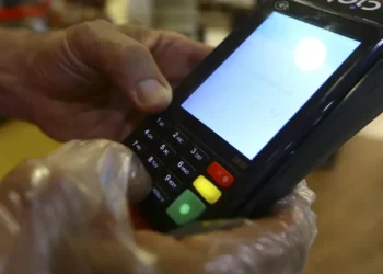 Pessoa digitando senha em maquininha de cartão com luva plástica