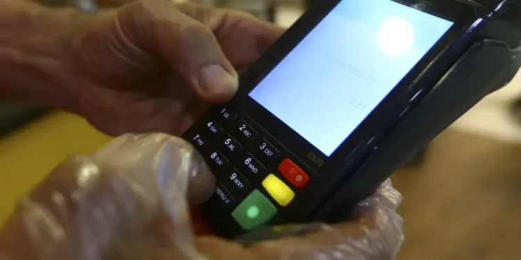 Pessoa digitando senha em maquininha de cartão com luva plástica