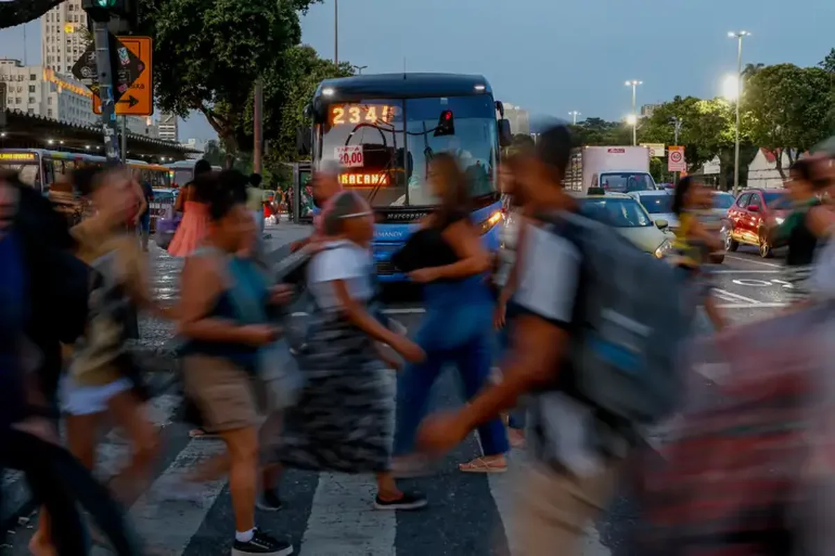 Trânsito intenso e pessoas atravessando a rua em horário de pico, em ambiente urbano.