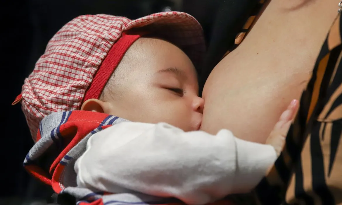 Bebê mamando no peito da mãe com roupa xadrez vermelha