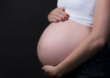 Mulher grávida segurando a barriga em fundo escuro