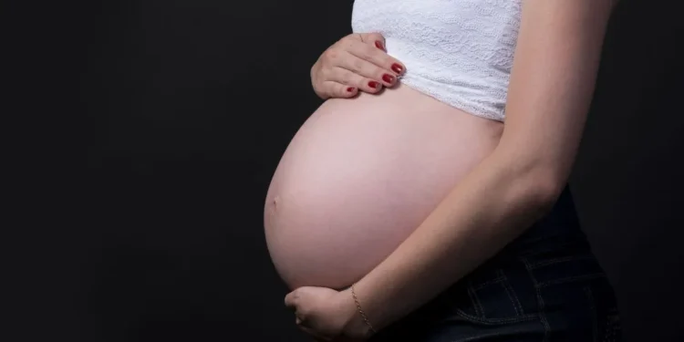 Mulher grávida segurando a barriga em fundo escuro