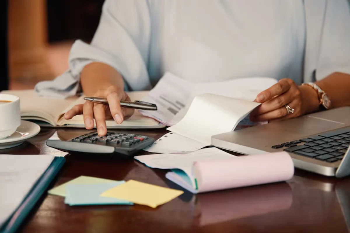 Pessoa calculando e organizando documentos relacionados ao pagamento de salário.