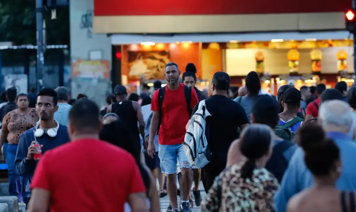 Imagem de uma multidão de pessoas caminhando pela rua, representando aqueles que podem ser beneficiados pelo novo salário de até R$ 1.630.
