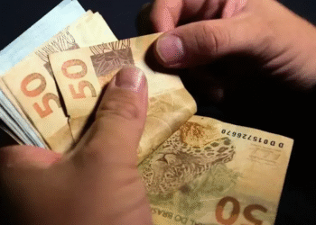 Imagem de uma pessoa segurando cédulas de 50 reais, simbolizando os valores a serem resgatados pelos brasileiros.