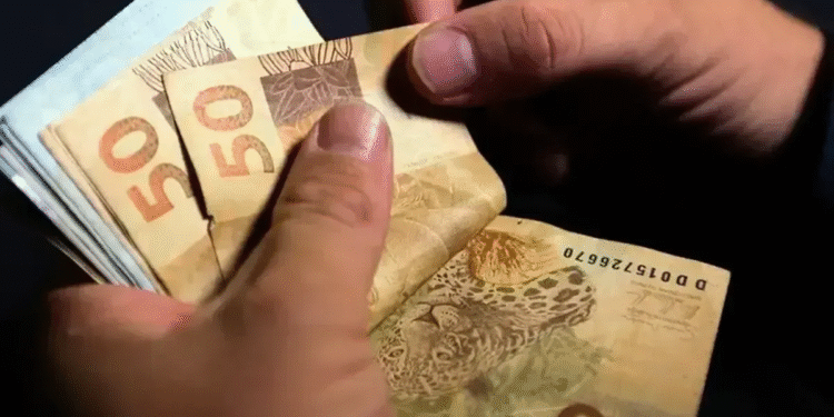 Pessoa contando cédulas de 50 reais, representando o recebimento da restituição do imposto de renda.