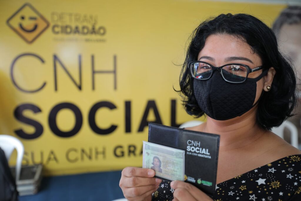 Beneficiária com a CNH Social. Mulher segurando a CNH Social, com o fundo exibindo o logo do Detran Cidadão.