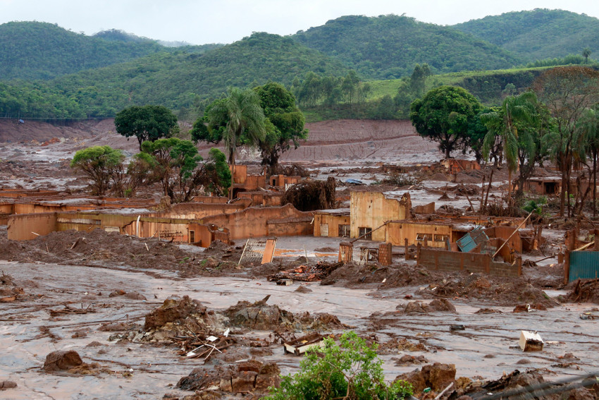 Paisagem devastada após o rompimento da Barragem do Fundão, com lama cobrindo vilas e áreas agrícolas.