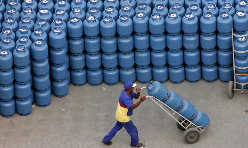 Trabalhador transportando botijões de gás em frente a depósito