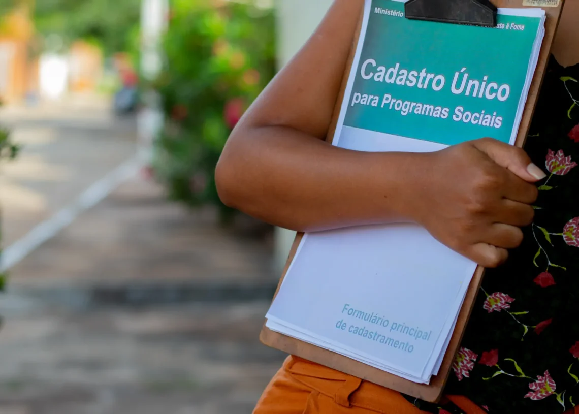 Pessoa segurando formulário do Cadastro Único para Programas Sociais, com foco em programas como o Bolsa Família.