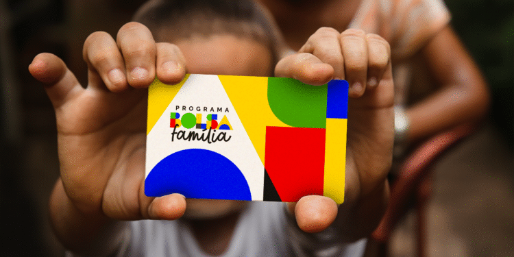 Mãos de uma criança segurando o cartão do programa Bolsa Família, com o novo design colorido e a logo do governo. A imagem representa o apoio financeiro e a inclusão social oferecidos a milhões de famílias no Brasil.