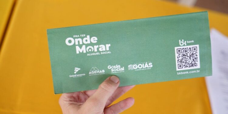 Pessoa segurando envelope verde do programa Aluguel Social de Goiás, auxilio aluguel com QR Code e logos de apoio.