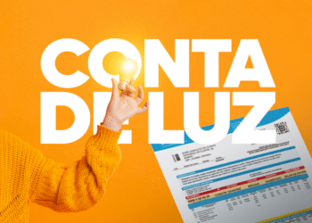 Mão segurando lâmpada acesa sobre uma conta de luz com o título "CONTA DE LUZ", ilustrando o aumento da tarifa com a bandeira vermelha.