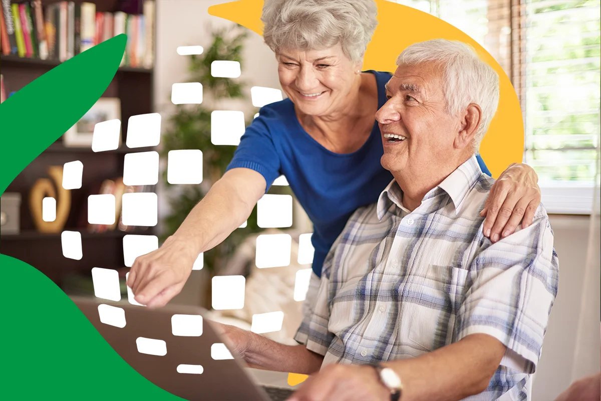 Casal de idosos sorrindo enquanto interagem com computador, ilustrando como consultar o calendário do INSS 2025.