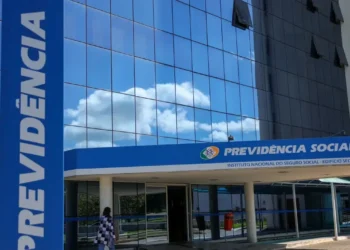 Imagem do prédio da Previdência Social, do Instituto Nacional do Seguro Social (INSS), com céu limpo ao fundo, em frente a uma pessoa caminhando.