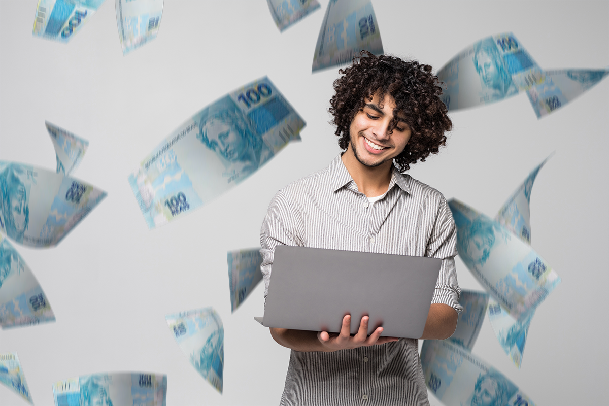 Homem sorrindo com um notebook, rodeado por notas de dinheiro, ilustrando ganhos financeiros mensais.