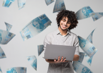 ovem sorridente segurando notebook com notas de 100 reais flutuando ao redor, representando o aumento do salário mínimo em 2026 para mais de R$ 1.600.