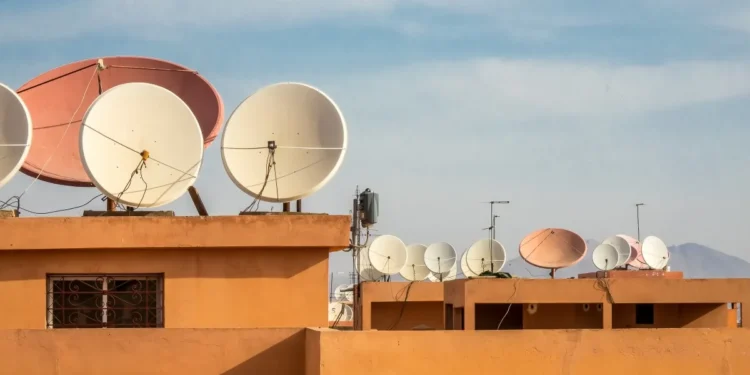 Antenas parabólicas em telhados de uma cidade, com diversas unidades de satélite.