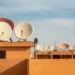 Antenas parabólicas em telhados de uma cidade, com diversas unidades de satélite.