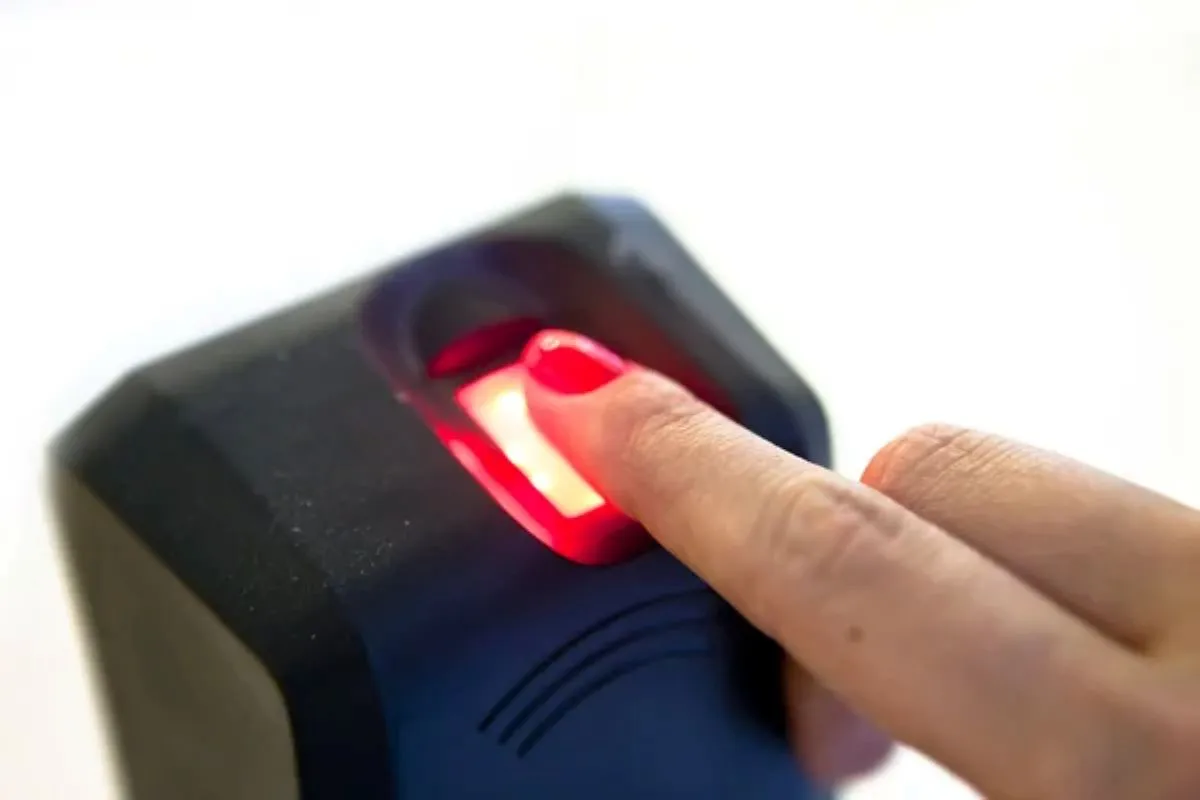 Pessoa utilizando um leitor biométrico para registrar suas impressões digitais, com foco na obrigatoriedade para a manutenção de benefícios sociais