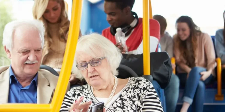 Imagem de idosos em um transporte público, com foco na tela do celular de uma idosa que interage com a interface, enquanto outros passageiros estão ao fundo.