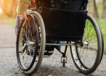 Pessoa utilizando cadeira de rodas em um caminho arborizado, representando beneficiários com deficiência do INSS.