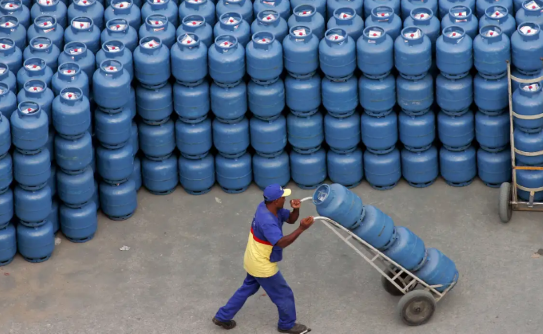 Imagem de um trabalhador transportando cilindros de gás azuis em um carrinho, ligado ao programa Gás do Povo.
