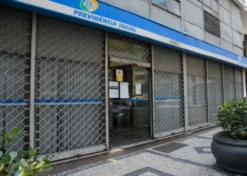 Agência do INSS com atendimento suspenso, visível pela grade de proteção e placas informativas.