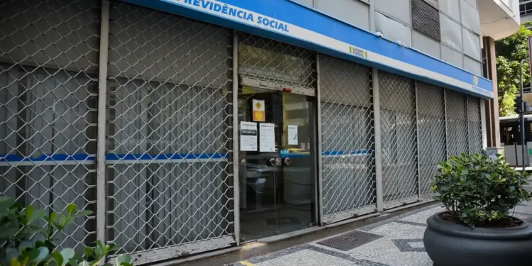 Agência do INSS com atendimento suspenso, visível pela grade de proteção e placas informativas.