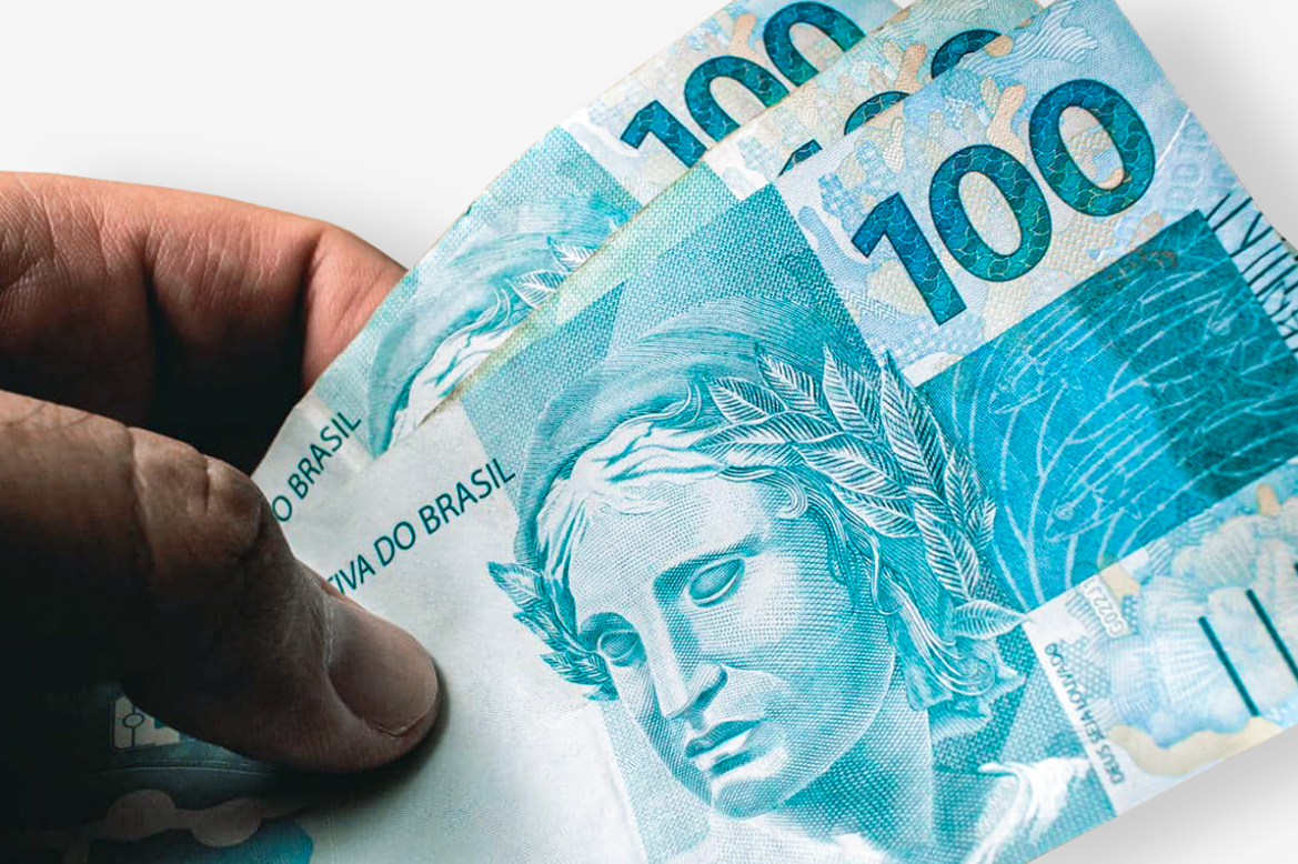 Cédulas de R$ 100 com a mão segurando, ilustrando o pagamento antecipado do Bolsa Família