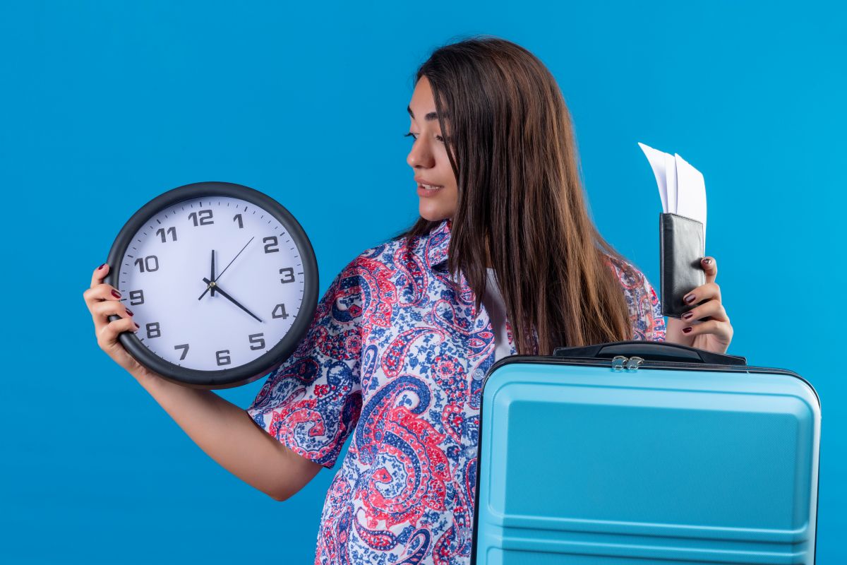 Mulher jovem com mala azul, bilhetes e relógio, representando contagem regressiva para o próximo feriado prolongado de 2025.