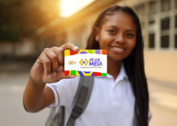 Pé de Meia 2025: Aluna exibindo cartão do programa com fundo de escola ao pôr do sol