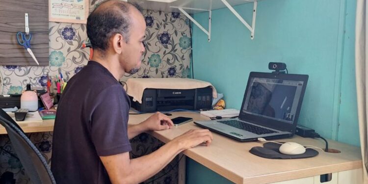 Homem utilizando notebook em chamada de vídeo com intérprete de Libras