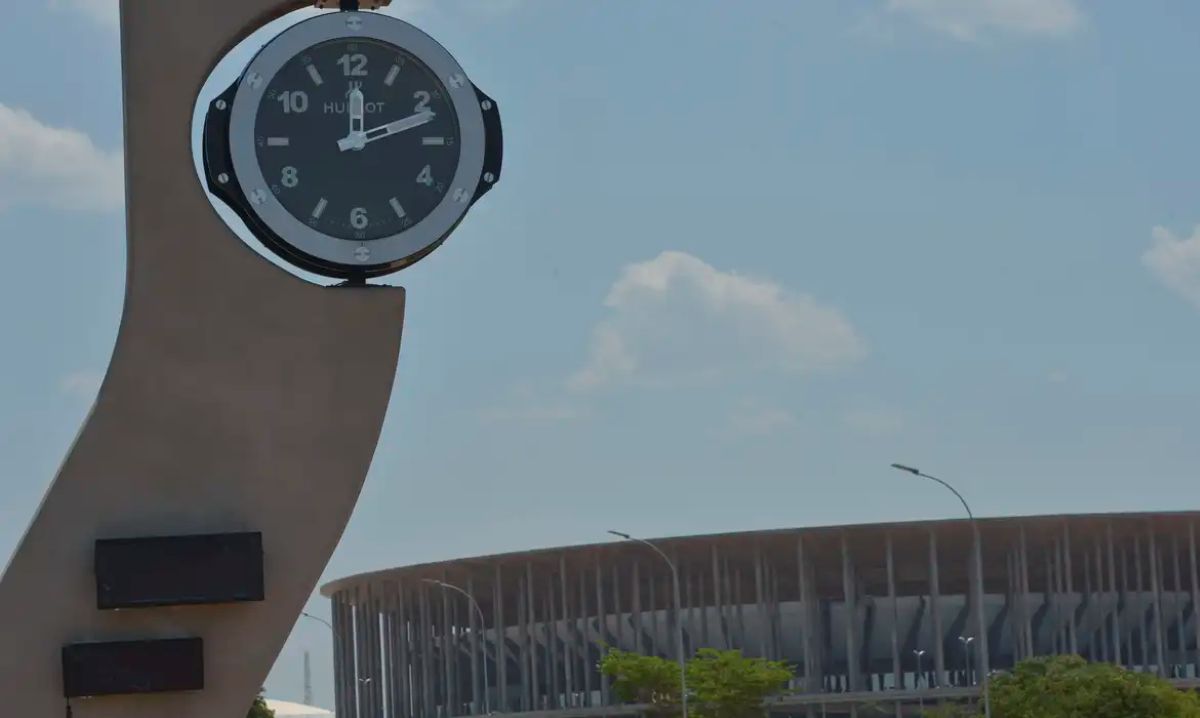 Relógio marcando o tempo próximo a um estádio, simbolizando a relevância do horário de verão em situações de emergência.