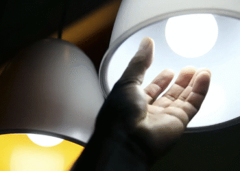 Mão estendida tocando luz branca de lâmpada LED circular com reflexos em superfície escura
