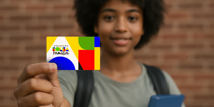 Jovem estudante segura o cartão do Bolsa Família em frente a uma parede de tijolos.