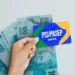 Cartão do PIS/PASEP da Caixa Econômica Federal sobre notas de R$ 100, simbolizando o saque dos valores.