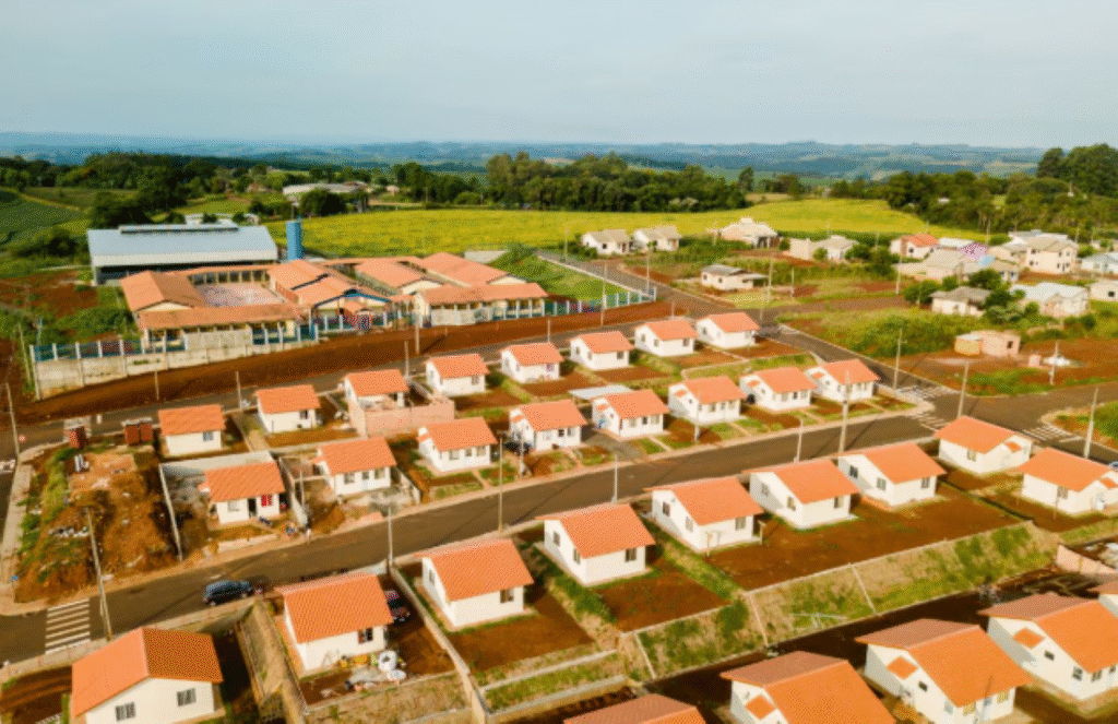 Vista aérea de um condomínio residencial moderno no programa Minha Casa, Minha Vida, com casas brancas de telhados vermelhos, áreas verdes e infraestrutura em desenvolvimento, ilustrando oportunidades de moradia acessível em 2025.