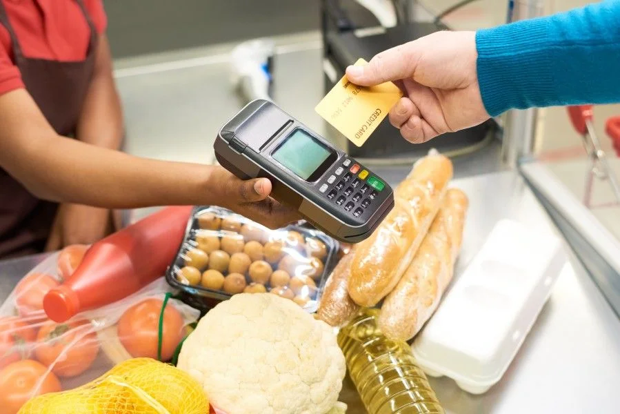 Pessoa fazendo pagamento com cartão de crédito em terminal de pagamento eletrônico (TEF) em supermercado, ilustrando a agilidade no processo de pagamento.