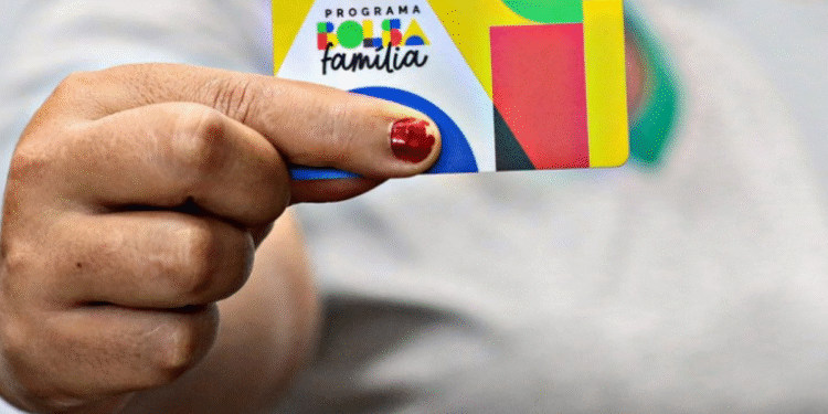 Mão segurando cartão do Programa Bolsa Família em fundo desfocado.
