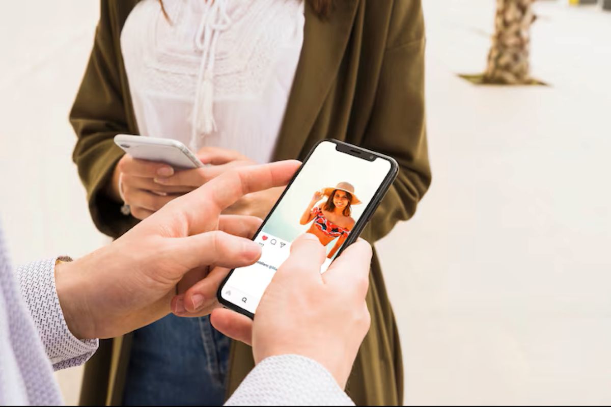 Duas pessoas em close-up, utilizando smartphones para navegar em redes sociais, com uma imagem de perfil de biquíni em destaque.